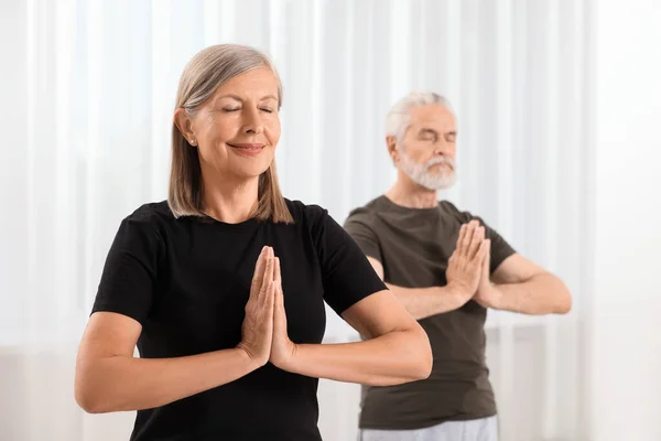 Senior couple practicing yoga indoors, selective focus