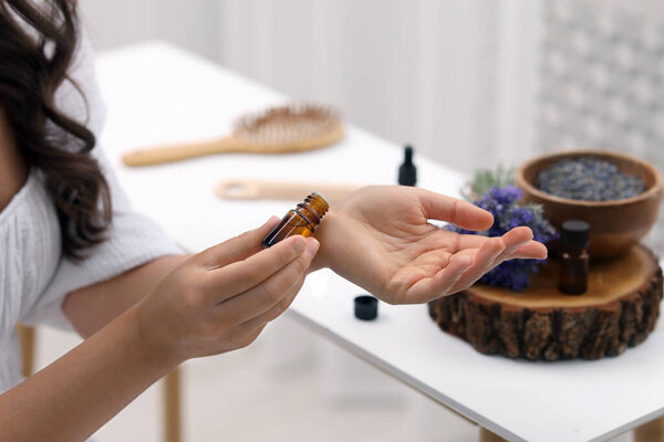 Woman with bottle applying essential oil onto wrist indoors, closeup