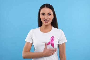 Açık mavi arka planda pembe kurdeleli güzel, mutlu bir kadın. Göğüs kanseri farkındalığı