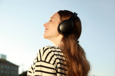 Kulaklıklı gülümseyen kadın dışarıda müzik dinliyor.
