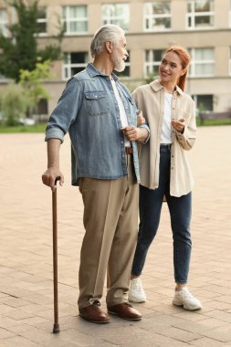 Bastonlu yaşlı adam ve açık havada genç bir kadın.