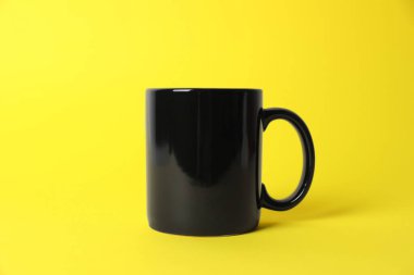 Sarı arka planda siyah bir seramik bardak.