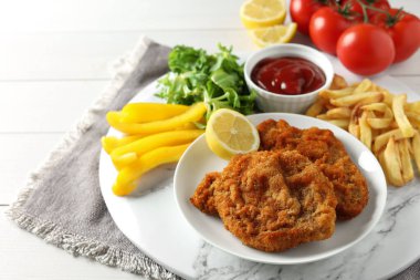 Patates kızartması, ketçap ve sebzelerle servis edilen lezzetli şnitzeller beyaz ahşap masada, yakın plan.
