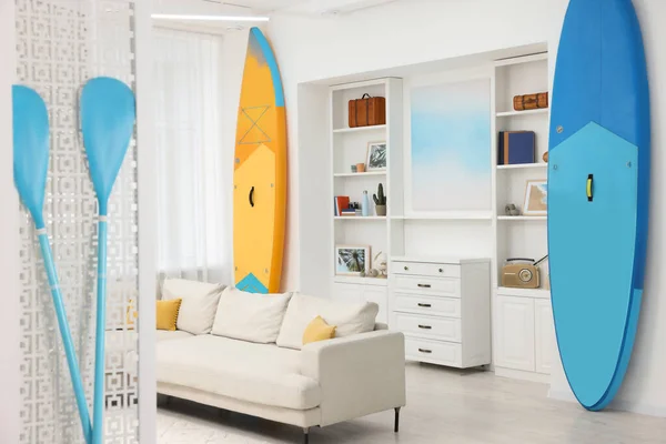 SUP boards, shelving unit with different decor elements and stylish sofa in room. Interior design