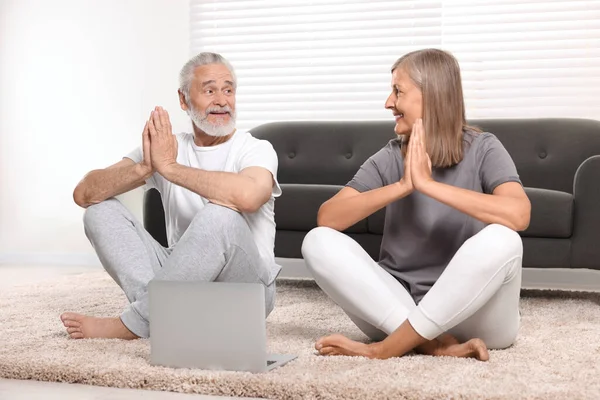 Senior couple practicing yoga with laptop at home
