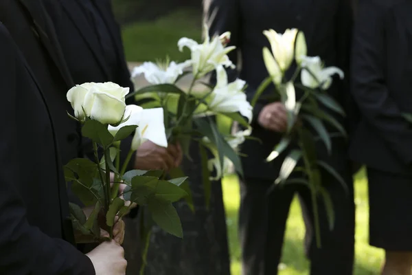 People with flowers outdoors, closeup. Funeral ceremony