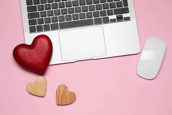 Laptop, computer mouse and decorative hearts on pink background symbolizing connection in long-distance relationship, flat lay
