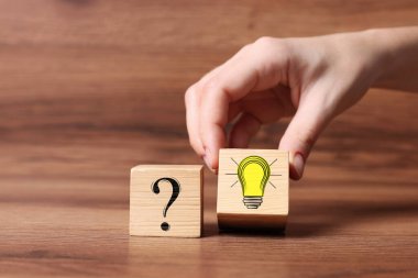 Fikir konsepti. Bir kadın, ahşap masa üzerinde soru işareti olan başka bir ampulü resmediyor, yakın plan.