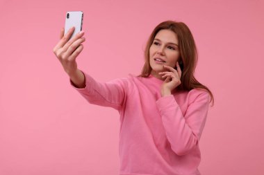 Güzel bir kadın pembe arka planda selfie çekiyor.