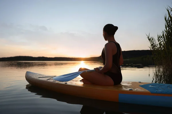 Woman paddle boarding on SUP board in river at sunset