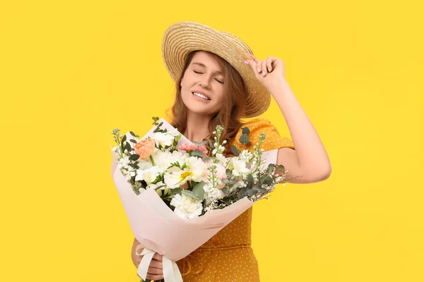 黄色の背景に美しい花の花束とわら帽子で幸せな女性 — ストック写真