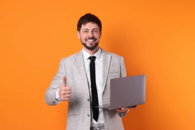 Bilgisayarlı mutlu adam turuncu arka planda baş parmağını gösteriyor.