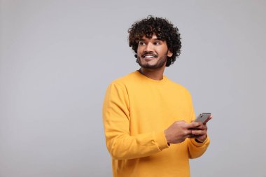 Açık gri arkaplanda akıllı telefon kullanan yakışıklı adam, metin için boşluk