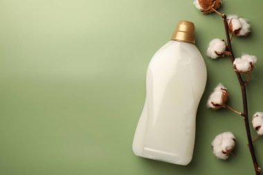 Bir şişe yumuşatıcı ve açık yeşil zemin üzerinde yumuşacık pamuk çiçekleri. Metin için boşluk