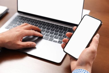 Masada akıllı telefon ve laptop kullanan adam, yakın plan.