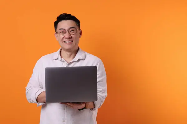 Happy man with laptop on orange background, space for text