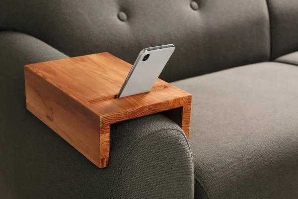 Smartphone on sofa with wooden armrest table in room, space for text. Interior element