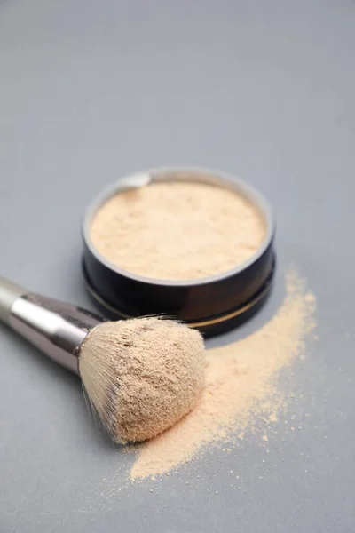 Loose face powder and makeup brush on light grey background, closeup