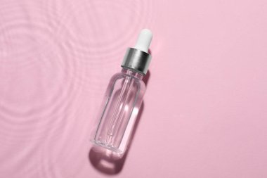 Pembe arka planda suda bir şişe kozmetik yağı.