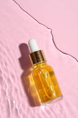 Pembe arka planda suda bir şişe kozmetik yağı.