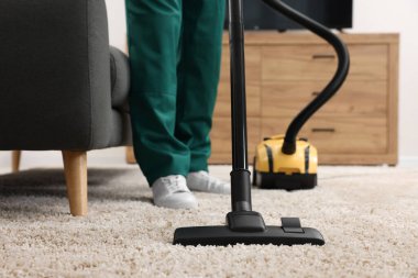 Kuru temizlemeci çalışanı halı süpürüyor, elektrikli süpürge içeride, yakın plan.