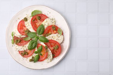 Beyaz fayanslı masa üzerinde pesto soslu bir tabak lezzetli Caprese salatası. Metin için boşluk
