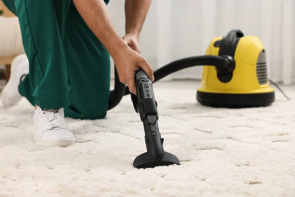 Dry cleaner's employee hoovering carpet with vacuum cleaner indoors, closeup