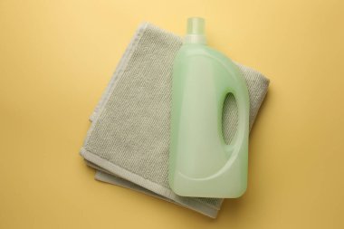 Bir şişe yumuşatıcı ve soluk sarı arka planda havlu, üst manzara.