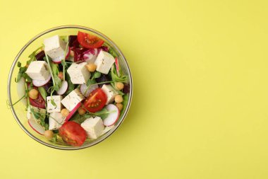 Sarı arka planda tofu ve sebzeli bir kase lezzetli salata, üst manzara. Metin için boşluk