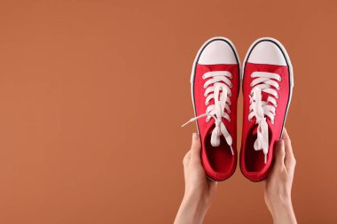Kahverengi arka planda klasik kırmızı spor ayakkabılı bir kadın, yakın plan. Metin için boşluk