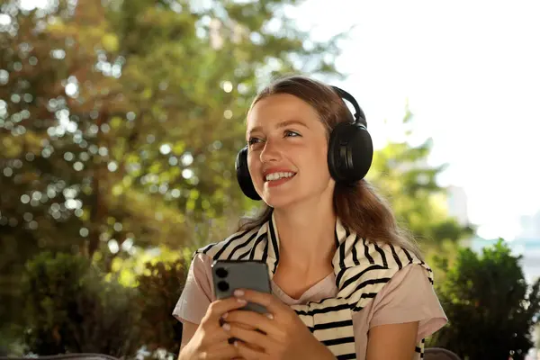 Smiling woman in headphones using smartphone outdoors