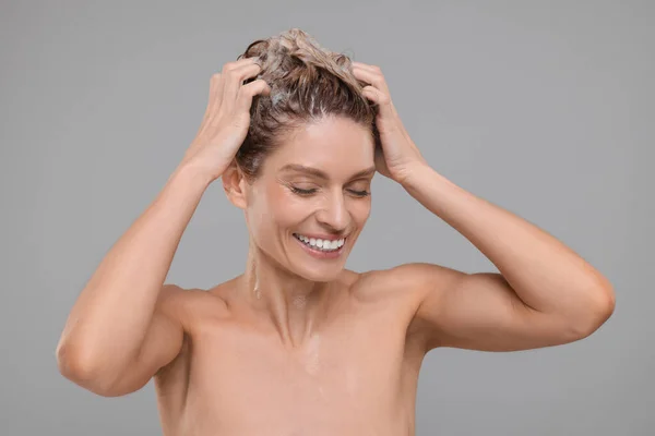 美丽而快乐的女人在浅灰的背景上洗头 — 图库照片