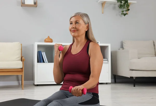 Senior woman exercising with dumbbells at home. Sports equipment