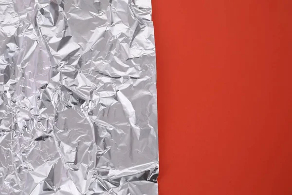 Sheet of crumpled aluminum foil on orange background, top view. Space for text