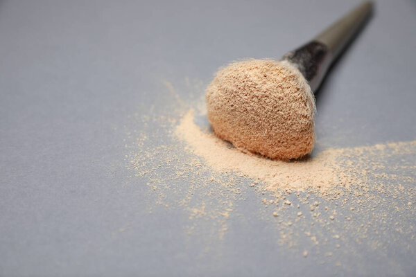 Loose face powder and makeup brush on light grey background, closeup. Space for text