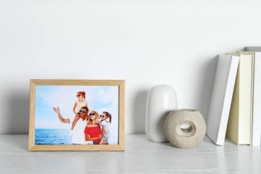 Beyaz ahşap masa üzerinde aile fotoğrafı, kitap ve dekor unsurları olan çerçeve