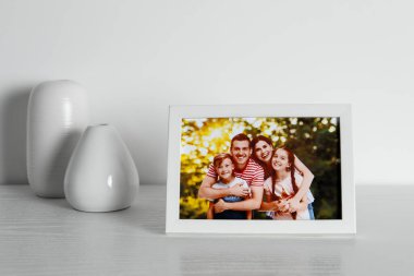İçinde aile fotoğrafı ve vazoların olduğu çerçeve beyaz ahşap masa içinde.