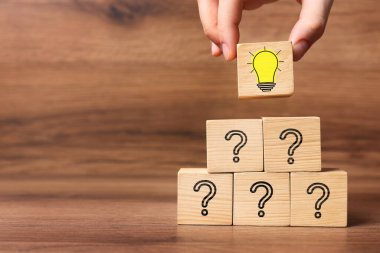 Fikir konsepti. Bir kadın, ahşap masa üzerinde soru işaretleri olanlara ampul resimleriyle küp yerleştiriyor, yakın plan.