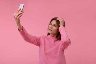 Güzel bir kadın pembe arka planda selfie çekiyor.