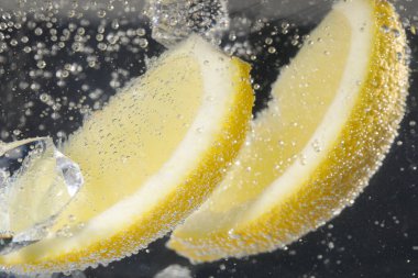 Sulu limon dilimleri ve buzlu soda, siyah arka planda, yakın plan.
