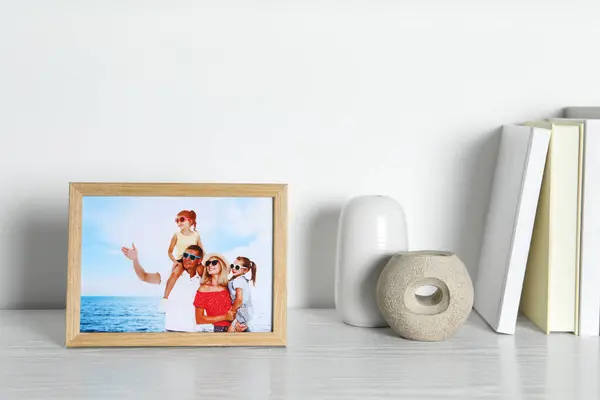 Frame with family photo, books and decor elements on white wooden table