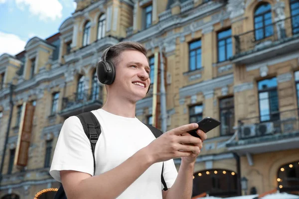 Smiling man in headphones using smartphone outdoors. Space for text