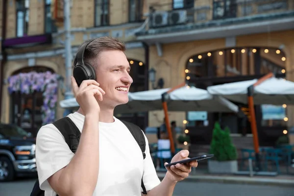 Smiling man in headphones using smartphone outdoors. Space for text