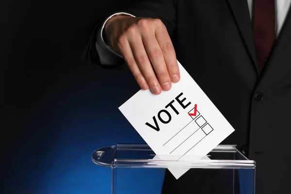 ダークブルーの背景に紙を投票して投票箱に入れる男 — ストック写真