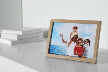 İçinde aile fotoğrafı ve beyaz ahşap masa üzerine kitaplar olan çerçeve.