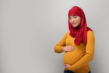 Açık gri arka planda tesettürlü hamile Müslüman kadın portresi, metin için boşluk