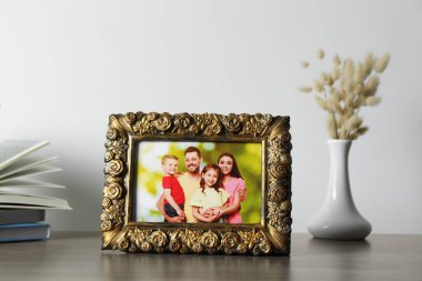 Aile fotoğrafı, kitaplar ve ahşap masa üzerinde kuru çiçek vazosu olan klasik kare çerçeve.