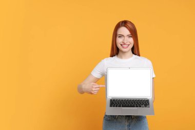 Sarı arka planda dizüstü bilgisayar gösteren gülümseyen genç kadın, mesaj için boşluk