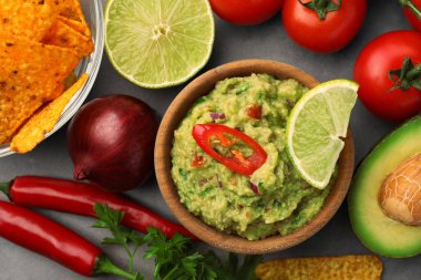 Bir kase lezzetli guacamole, cips ve malzemeler gri masada, düz yerde.