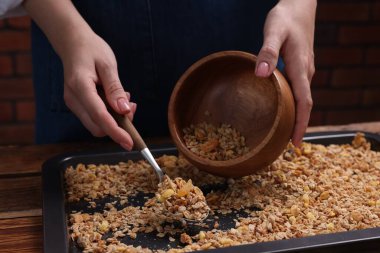 Bir kadın yemek tepsisinden kaseye granola koyuyor, yakın plan.